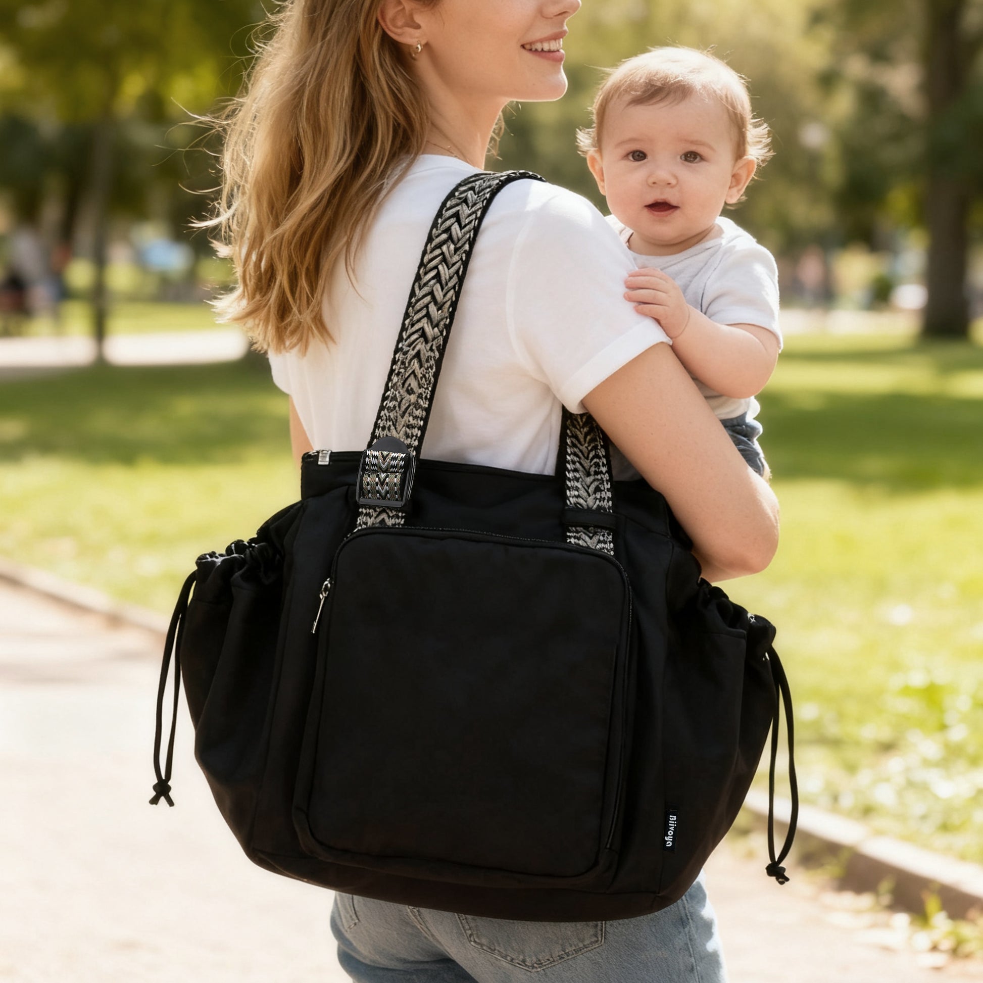 Woman carrying a black backpack with a baby on a path in a park