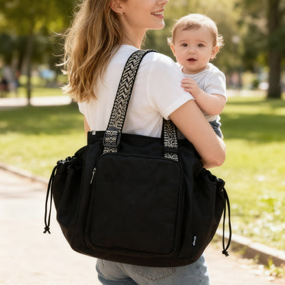 Woman carrying a black backpack with a baby on a path in a park