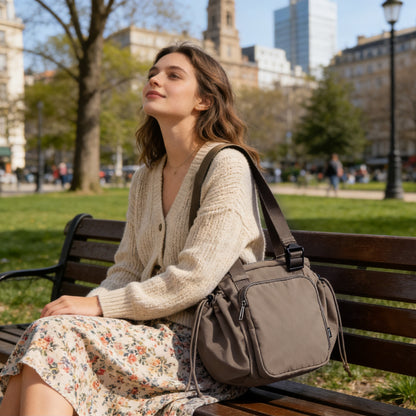 Woman sitting on a park bench with a large brown bag, surrounded by trees and buildings.